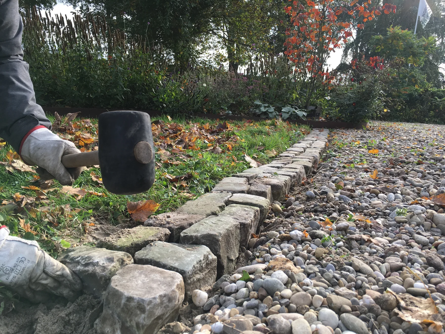 Handen leggen een lage rand van gebakken stenen in de tuin.